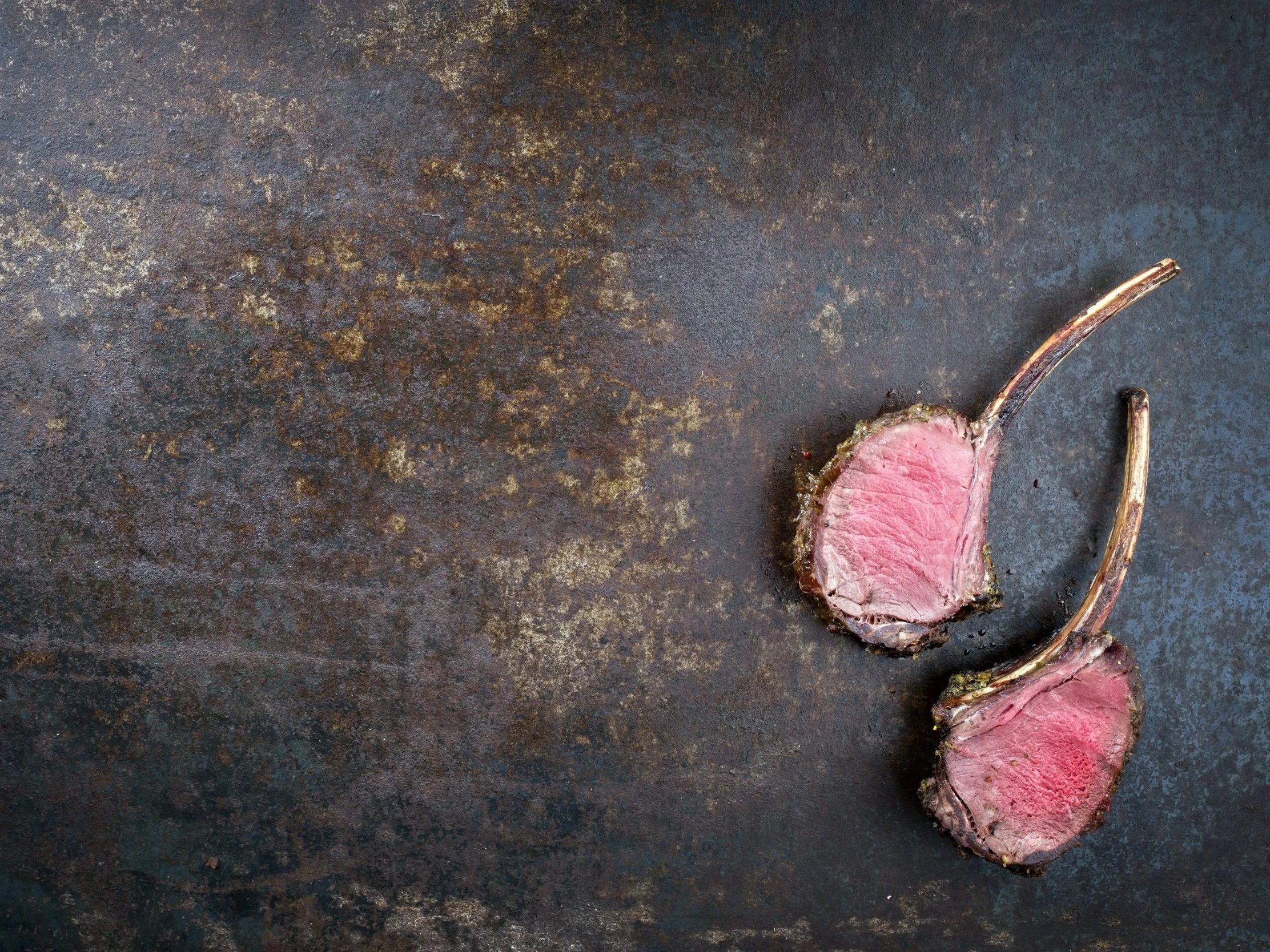 Juicy, perfectly cooked lamb chops with a pink center resting on a rustic metal surface, showcasing a gourmet presentation ideal for culinary blogs and recipes.